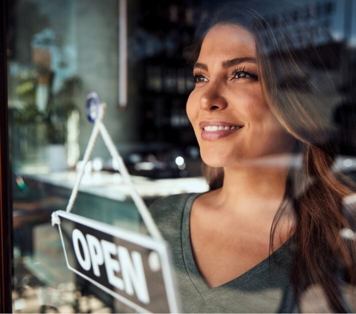 Restaurant owner smiling beside an open sign in her doorway, illustrating the UAE food and beverage industry