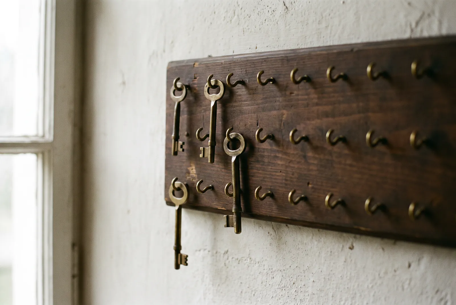 Wooden key board on a plaster wall with three brass keys hanging among rows of empty hooks