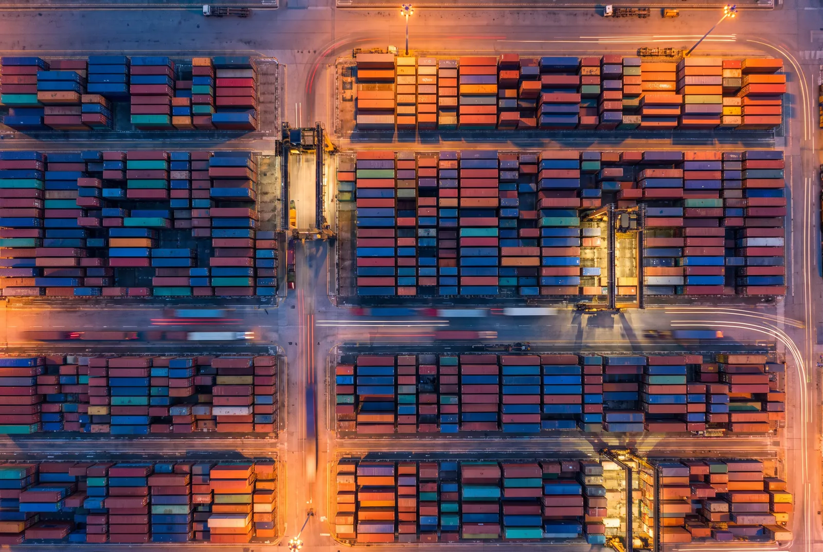 Aerial view of a container port yard at blue hour with light trails between stacked containers